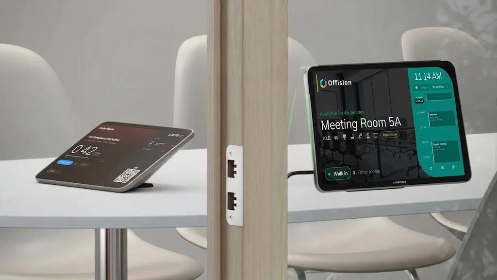 An Offision check-in tablet on a meeting table beside a Crestron door panel showing Meeting Room 5A available, with ethernet ports on the wood pillar between them