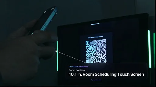 Hand scanning a QR code on a Crestron room scheduling panel with green status lights